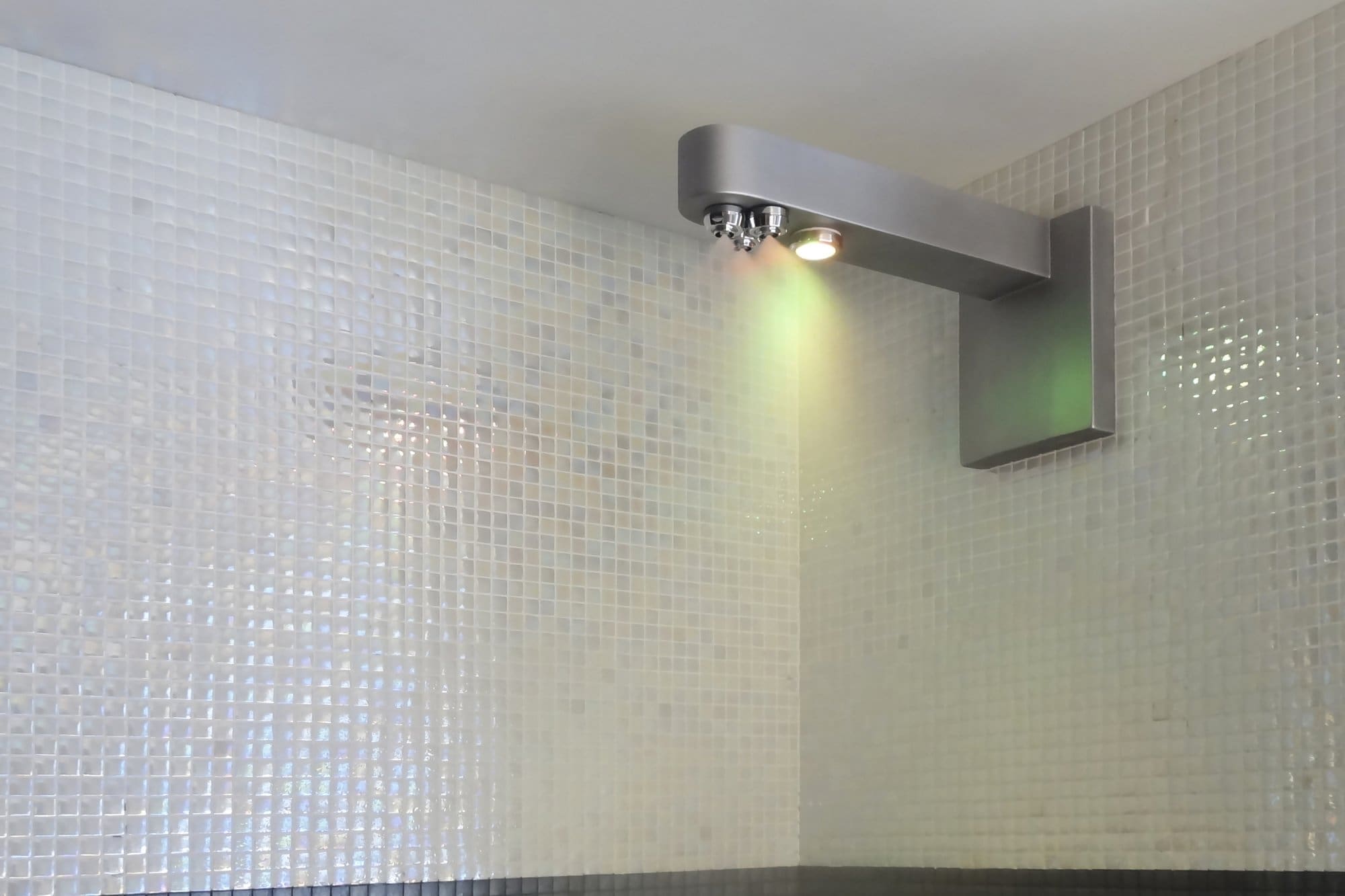 Ducha nebulizante bitermica con cromoterapia de color verde en pared de mosaico.